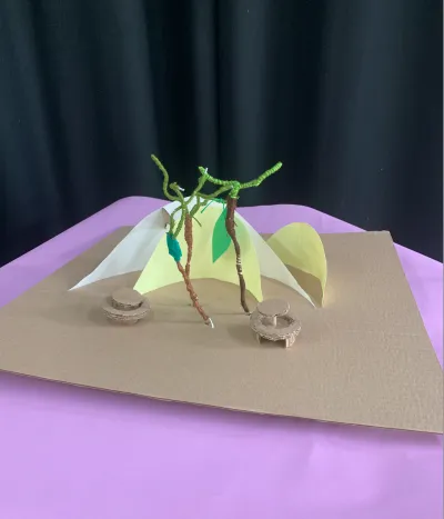 Cardboard structures of trees and seating on a flat purple background.