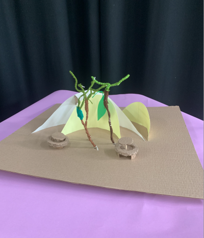 Cardboard structures of trees and seating on a flat purple background.