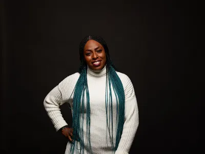 Young woman wearing a white polo neck jumper smiles at the camera with hand of her hip