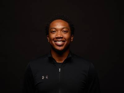 young man wearing a black zip up top smiles at the camera