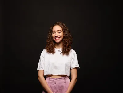 young woman wearing pink trousers smiles at the camera