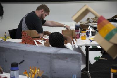 2 people pictured painting cardboard structures