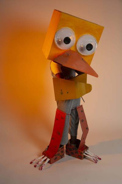 Large cardboard duck costume posing on a yellow backdrop