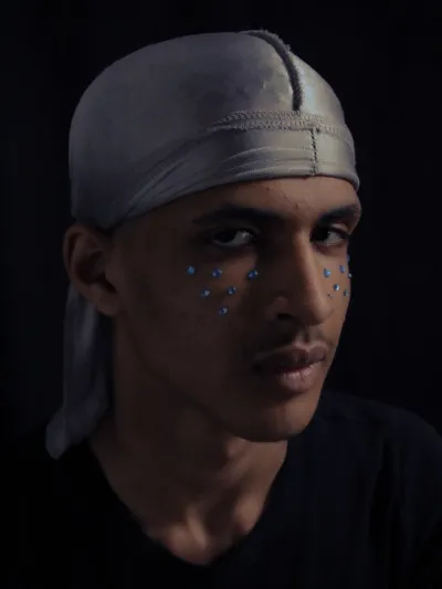 Young man wearing a white do-rag with silver sparkles on his cheeks