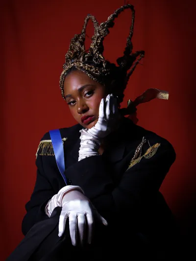 Young woman dressed royally poses with her hand on her cheek