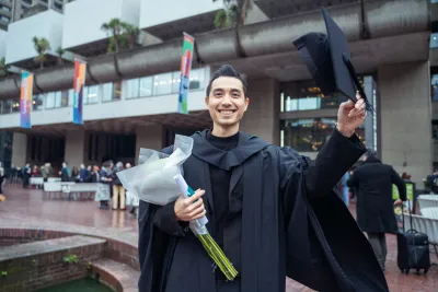 Graduate lifts his cap while holding a bouquet of flowers
