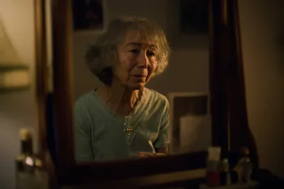 A mirror with a lady's reflection. The lady is looking at herself in the mirror, her expression is sorrowful. 