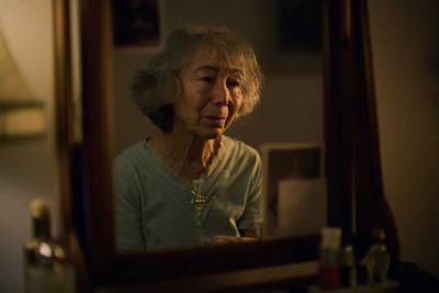 A mirror with a lady's reflection. The lady is looking at herself in the mirror, her expression is sorrowful.
