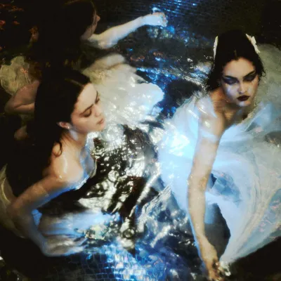 Birds eye view of women in white dresses swimming in dark water.