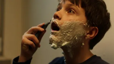 Boy with shaving foam on his face, looking up and shaving.