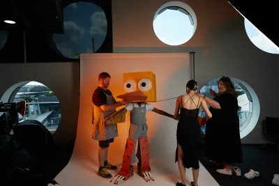 3 people fixing a large robotic duck costume in a photography studio